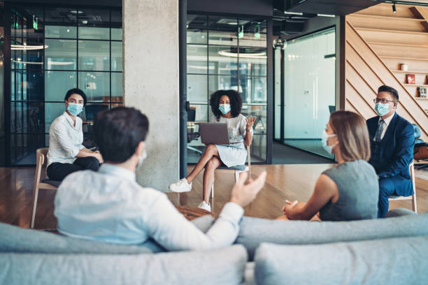 Group of entrepreneurs on a meeting during the pandemic Group of entrepreneurs, wearing masks, sitting at a distance in the office and talking small group of people photos stock pictures, royalty-free photos & images