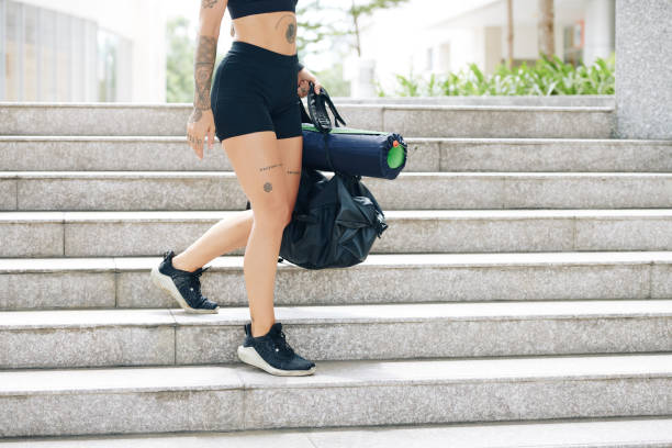 Woman going to gym Cropped image of fit young woman in shorts and sports bra walking down the stairs with gym bag in hands cycling shorts stock pictures, royalty-free photos & images