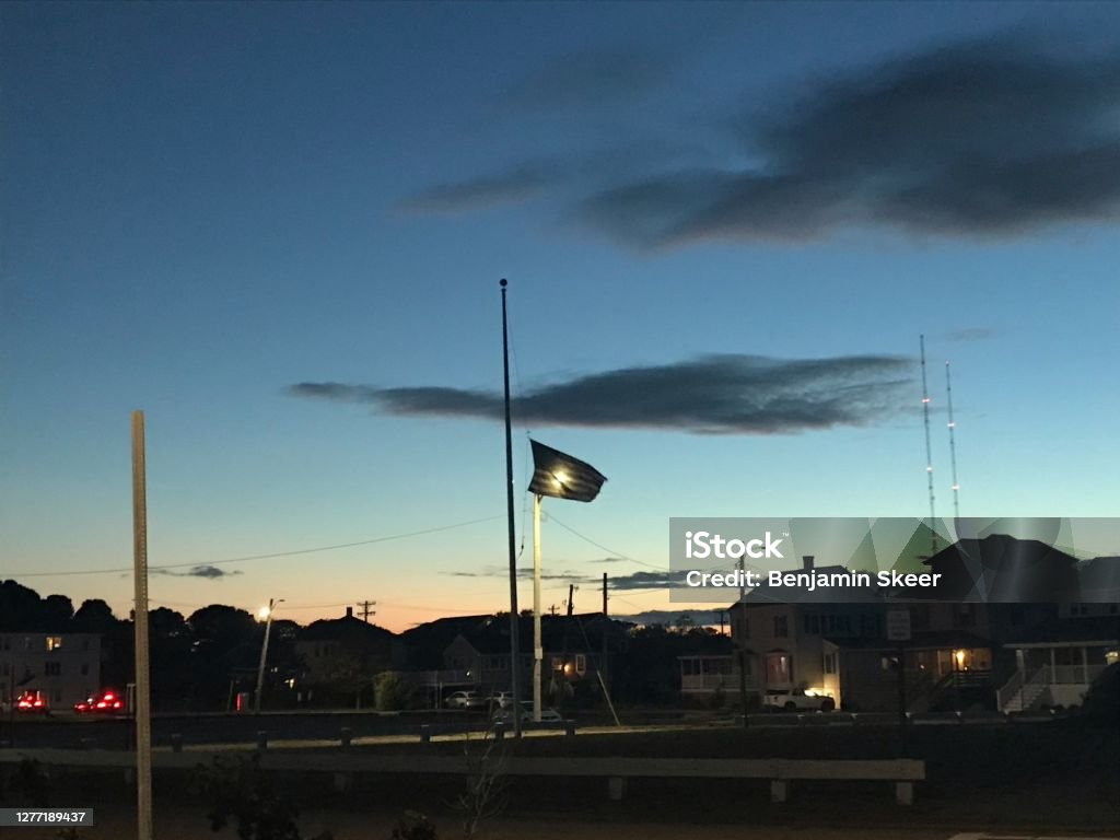 An American Flag at half mast Sunset An American flag at half mast for Ruth Bader Ginsberg  illuminated by a Streetlight with dark clouds overhead. American Flag Stock Photo