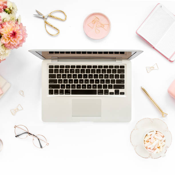 istock Stylized women's home office desk. Workspace with laptop, computer, bouquet ranunculus and roses, clipboard on white background. Flat lay. Top view 1277191077