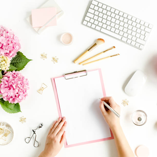 istock Female workspace with female hands, clipboard, bouquet hydrangea, computer, accessories on white background. Stylized women's desk. Flat lay. Top view 1277191840