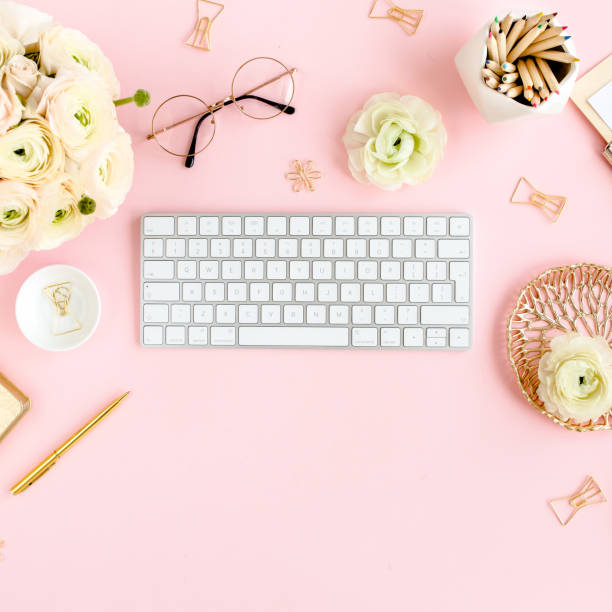 istock Stylized, pink women's home office desk. Workspace with computer, bouquet ranunculus and roses, clipboard on pink background. Flat lay. Top view 1277192460