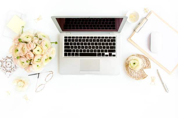 istock Stylized women's home office desk. Workspace with laptop, computer, bouquet ranunculus and roses, clipboard on white background. Flat lay. Top view 1277193619