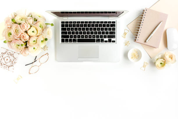 istock Stylized women's home office desk. Workspace with laptop, computer, bouquet ranunculus and roses, clipboard on white background. Flat lay. Top view 1277193973