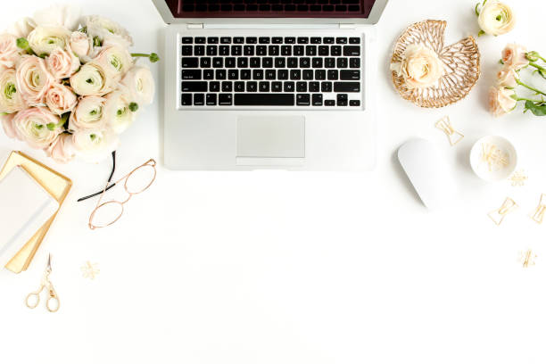 istock Stylized women's home office desk. Workspace with laptop, computer, bouquet ranunculus and roses, clipboard on white background. Flat lay. Top view 1277194099