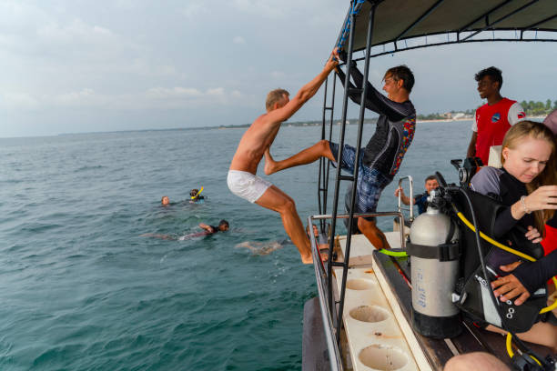 a man is jumping into the sea from a board of a boat and has fun. - men latin american and hispanic ethnicity southern european descent mature adult imagens e fotografias de stock