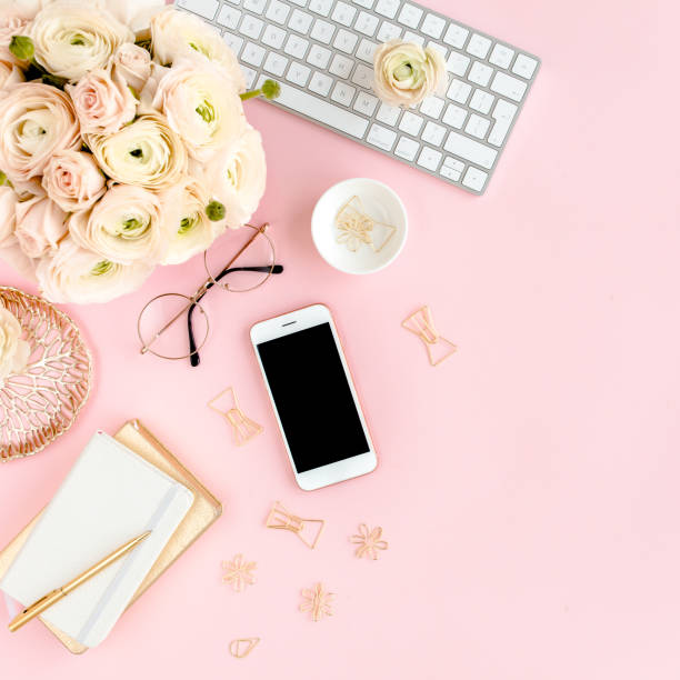 istock Stylized, pink women's home office desk. Workspace with computer, bouquet ranunculus and roses, phone on pink background. Flat lay. Top view 1277195425