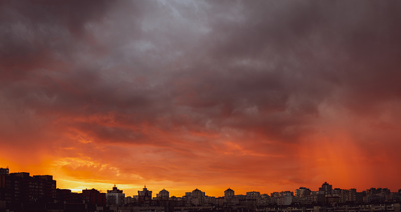 Wide-angle shot of dramatic stormy sunset sky with clouds over the city skyline background.