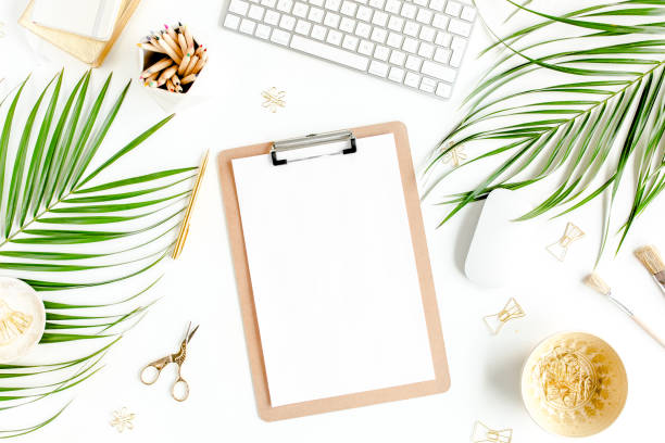 Flat lay home office desk. Female workspace with computer, clipboard, tropical palm leaves, accessories on white background. Top view