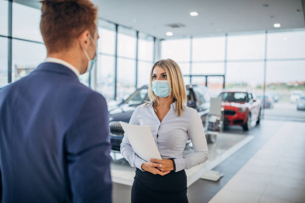 Young female car dealer and young male customer with protective face masks talking in a car showroom Young female car dealer and young male customer with protective face masks talking in a car showroom. car salesperson photos stock pictures, royalty-free photos & images