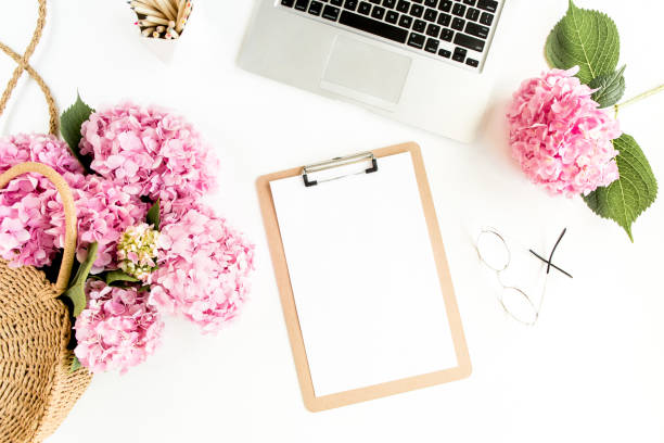 Stylized women's desk. Workspace with clipboard, laptop, bouquet hydrangea, accessories on white background. Flat lay. Top view