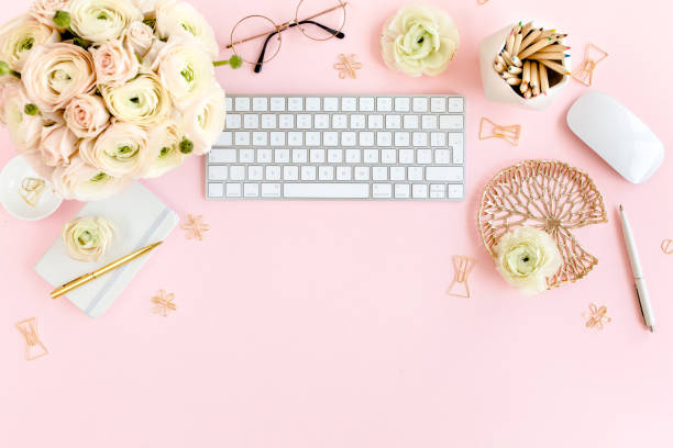 istock Stylized, pink women's home office desk. Workspace with computer, bouquet ranunculus and roses, clipboard on pink background. Flat lay. Top view 1277197032