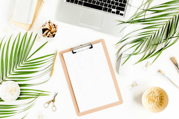 istock Flat lay home office desk. Female workspace with computer, clipboard, tropical palm leaves, accessories on white background. Top view 1277198239