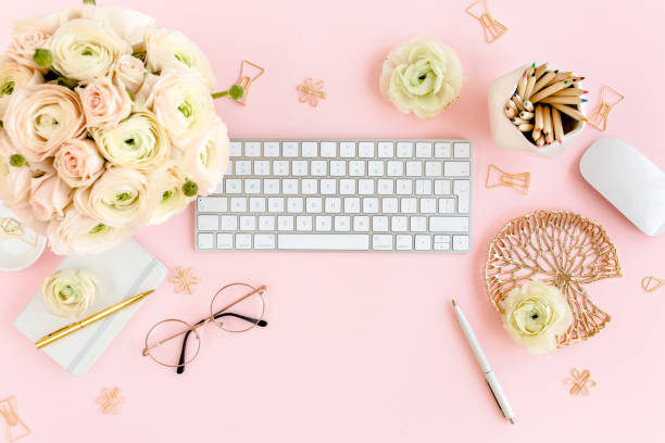 istock Stylized, pink women's home office desk. Workspace with computer, bouquet ranunculus and roses, clipboard on pink background. Flat lay. Top view 1277198358