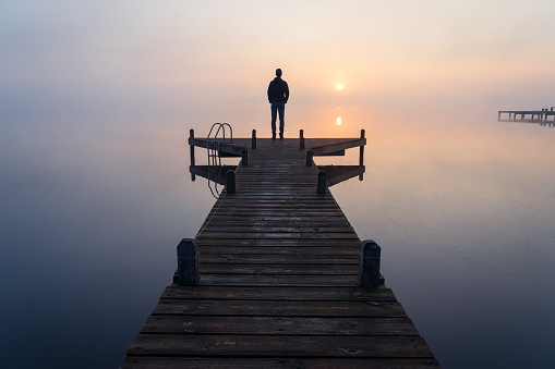 A man looking at the sunrise on a foggy, tranquil morning.