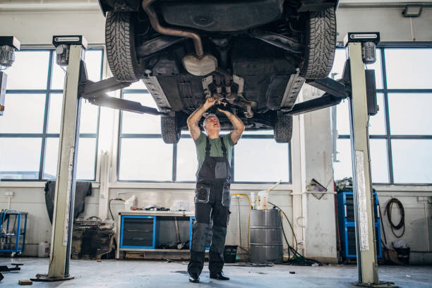 Mature man working on a vehicle in auto repair shop One man, mature man mechanic, working alone on a vehicle in car repair shop. mechanic working under car stock pictures, royalty-free photos & images