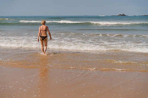 A mature woman bathes in the ocean on a beach in Bentota, Sri Lanka,