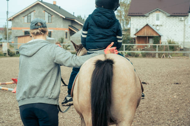 A child with special needs is riding with a close supervision teacher. This is a treatment called Hippotherapy, Life in the education age of disabled children, Happy disability kid concept. quarantine stock photo