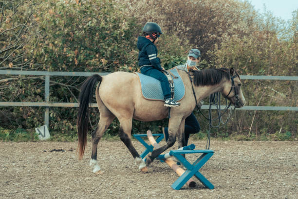 특별한 도움이 필요한 어린이는 가까운 감독 교사와 함께 타고있습니다. 이것은 하마 테라피, 장애아동의 교육 연령, 행복한 장애 아동 개념이라는 치료법입니다. 격리 - teaching child horseback riding horse 뉴스 사진 이미지