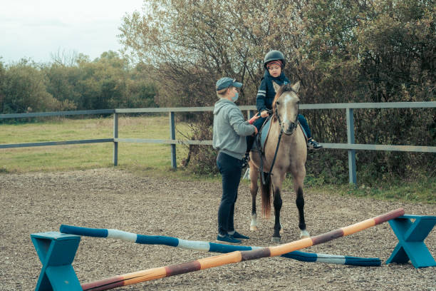 a child with special needs is riding with a close supervision teacher. this is a treatment called hippotherapy, life in the education age of disabled children, happy disability kid concept. quarantine - teaching child horseback riding horse imagens e fotografias de stock
