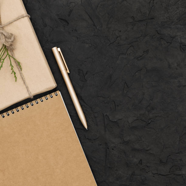 istock One gift wrapped in a craft paper and a twine. A notepad and a pen on black concrete background. Copy space, top view, flat lay, square. 1277205866