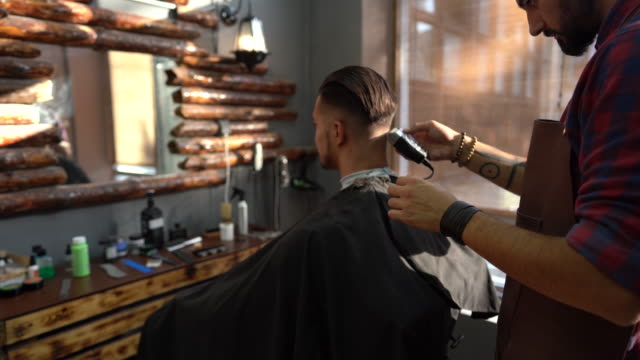 Barber trimming man's hair with electric razor in barber shop