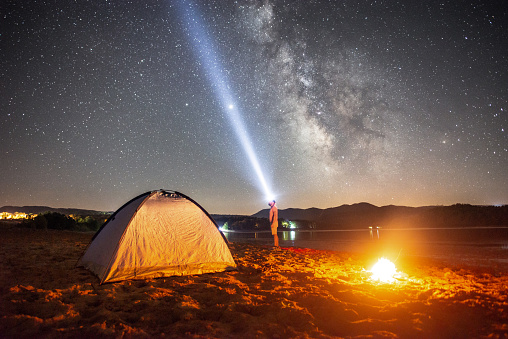 An illuminated tent under Milky Way in the mountain. Lonely man looking the bright night sky and the milky way near the lake