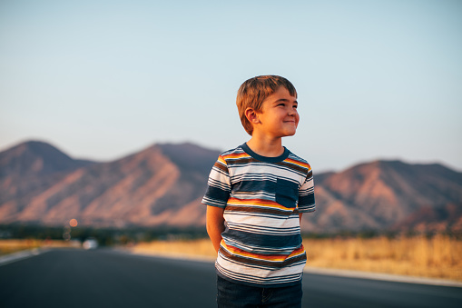 A young boy looks into the distance imagining the future and what life's experiences will bring. He stands on a rural road in Utah at sundown.