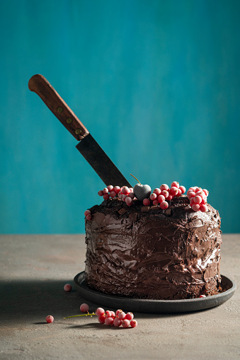 Chocolate cake with red currant frozen berries on top and cutting knife vintage on blue background