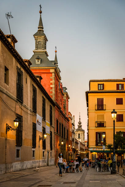 August, 2020. Madrid, Spain. The Plaza de Comendaras square in the old town, Conde Duque neighbourhood, with various people enjoying the evening in a terrace. A woman walking a dog.