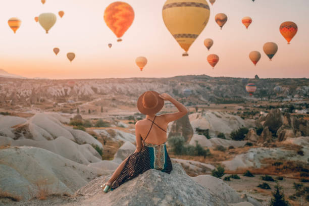 back view ung vuxen kvinna som sitter på marken tittar ballonger tittar på dalen. takadociens soluppgång - kvinna ballonger bildbanksfoton och bilder