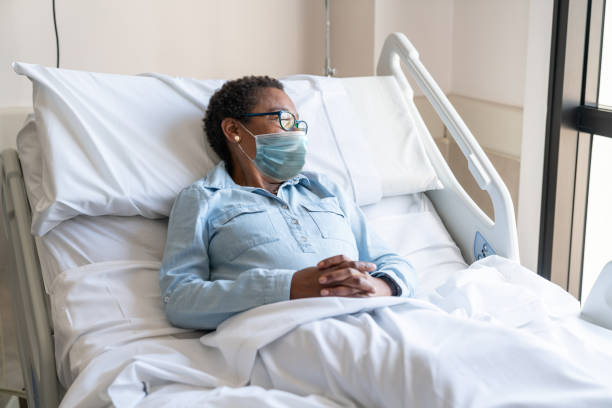 Female black hospitalized patient lying in bed looking away while wearing a protective facemask Female black hospitalized patient lying in bed looking away while wearing a protective facemask - Lifestyles hospital depression sadness bed stock pictures, royalty-free photos & images