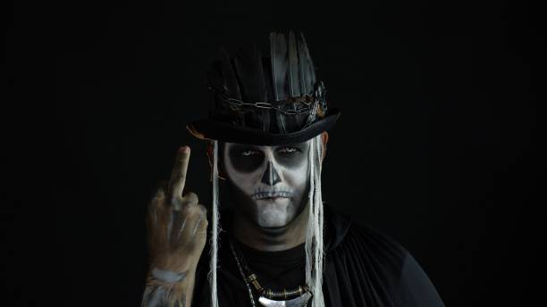 istock Sinister man with skull makeup making faces and showing middle finger. Bad manner gesture. Halloween 1277232411