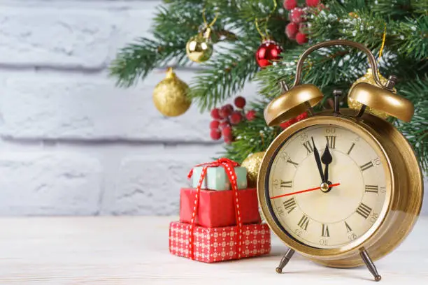 Christmas tree and countdown to the new year. Bronze retro clock, gift boxes and balls and fir spruce branches on white brick background with copy space.