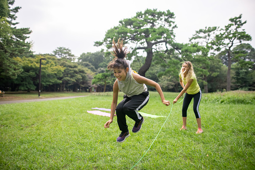 Teenage girl playing with jumping rope with mother in public park