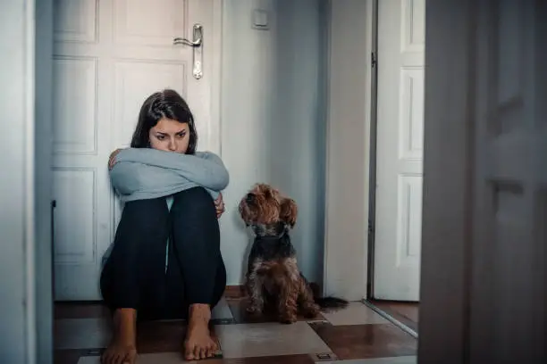 Woman with mental health problems is sitting desperate on the floor and  crying and her dog is next to her