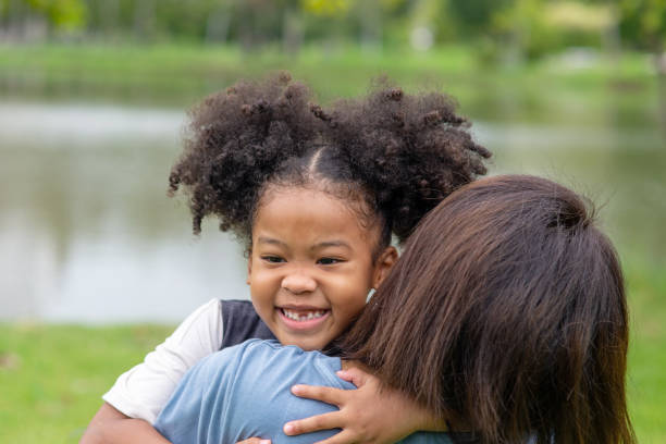 happy affectionate mixed race family. cute child girl embrace her mother with toothy smile in the park. mom and little daughter enjoy spending time together in summer outdoor weekend holiday vacation. - offspring child toothy smile beautiful imagens e fotografias de stock