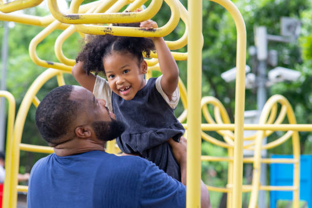 Happy affectionate mixed race family. African man father carrying little daughter playing at playground in the park. Dad and cute child girl enjoy and having fun together in outdoor weekend vacation. Happy African father carrying little daughter playing at playground in the park. playground stock pictures, royalty-free photos & images