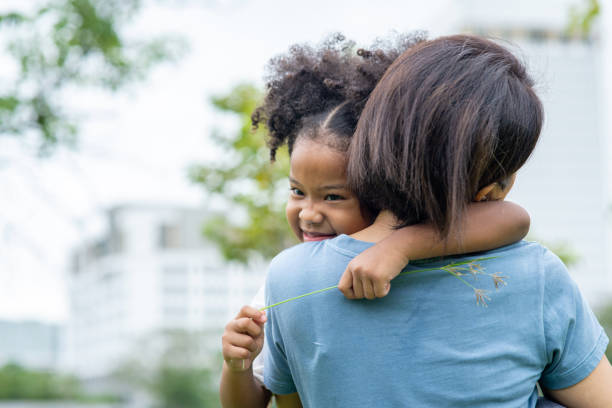 glückliche liebevolle gemischte rasse familie. nettes kleines kind mädchen umarmen ihre mutter mit zu schüchternen lächeln. mama trägt tochter und verbringen zeit zusammen im sommer outdoor-wochenende urlaub. - offspring child toothy smile beautiful stock-fotos und bilder