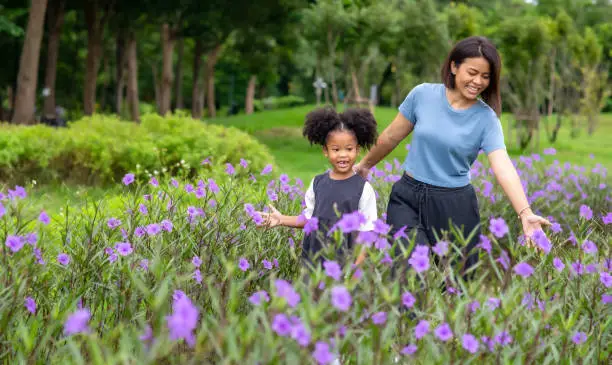 Photo of Happy mixed race family mother with little daughter holding hands and walking together in the garden. Smiling mom with cute child girl  enjoy and having fun in summer outdoor weekend holiday vacation