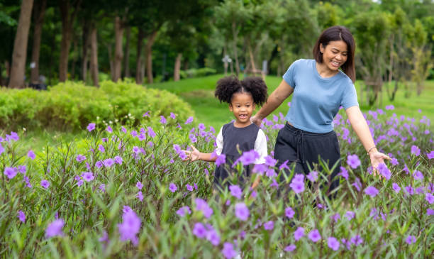 幸福的混血家庭母親帶著小女兒牽著手,一起在花園裡散步。微笑媽媽與可愛的女孩享受和樂趣在夏季戶外週末假期。 - 單親家庭 圖片 個照片及圖片檔