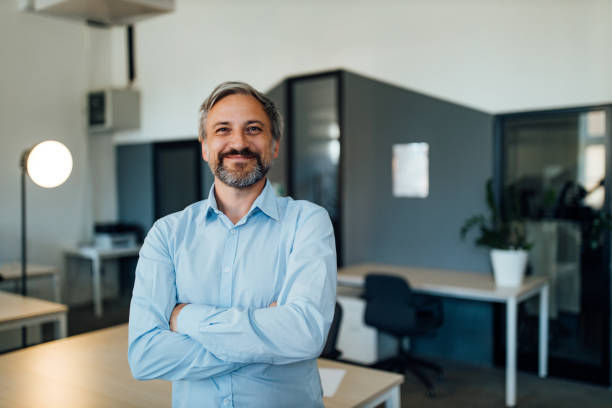 Man looking at camera, posing for picture. Businessman standing in his office. business person one man only blue standing stock pictures, royalty-free photos & images