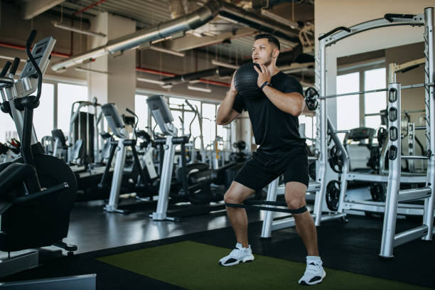 Man holding ball and doing squats. Man doing exercises, using balls and exercise tape. health club photos stock pictures, royalty-free photos & images