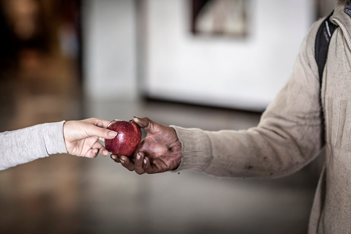 Detail of hand of young woman giving an apple to homeless person