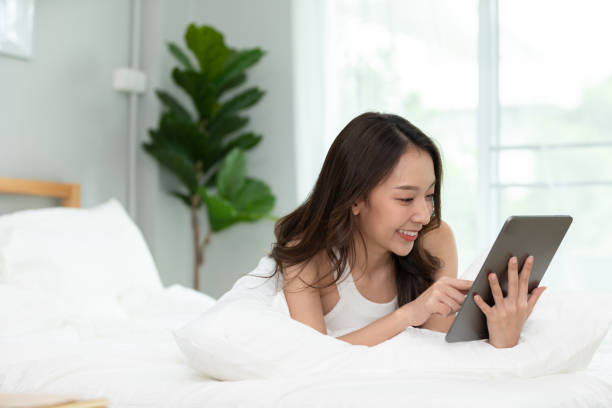 istock Beauty Asian woman smile and using computer tablet on her bed at home,using social media and multimedia on tablet relax in holiday 1277250042