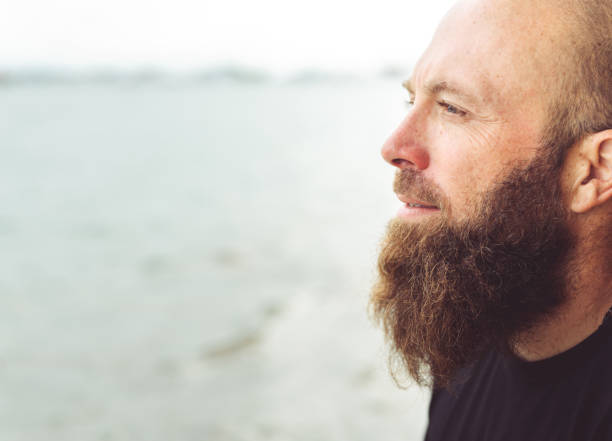 istock Man with beard at the beach looking off into the distance 1277252963