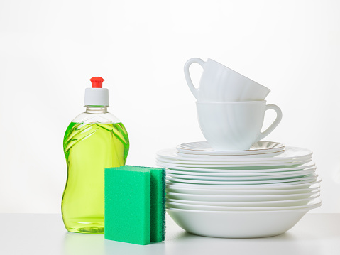 A set of clean dishes, gel and a set of foam sponges on a white table. The concept of cleaning and maintaining cleanliness.