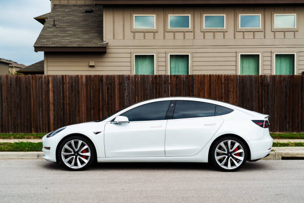 Portrait view of the Tesla Model 3 Austin, TX, USA - September 15, 2020:White Tesla Model 3 The American Made Electric sports car parked in the suburbs of Austin , Texas , USA next to the street side and large wooden fence and big two story suburban house tesla model 3 stock pictures, royalty-free photos & images