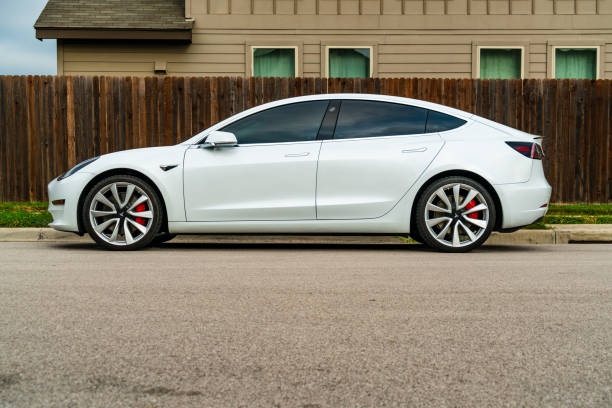 The Tesla Model 3 in White in the Suburbs of Austin , Texas Austin, TX, USA - September 15, 2020:White Tesla Model 3 The American Made Electric sports car parked in the suburbs of Austin , Texas , USA next to the street side and large wooden fence and big two story suburban house tesla model 3 stock pictures, royalty-free photos & images
