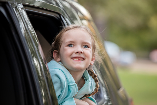 Child with pigtails looks out car window and smiles
